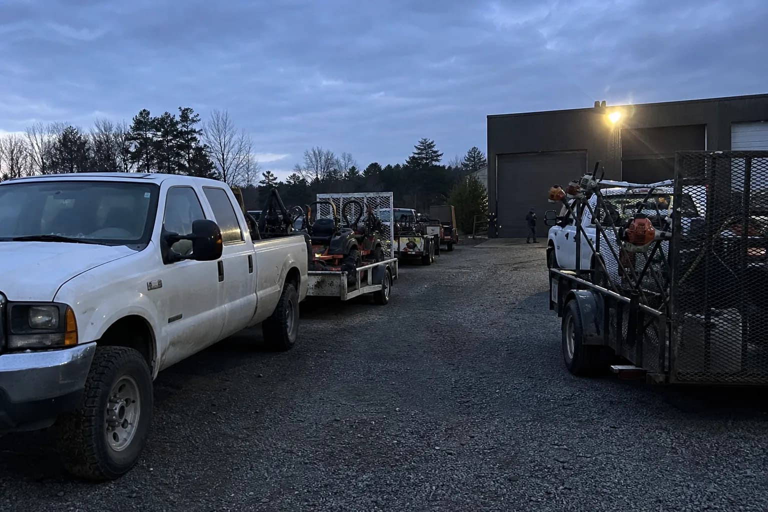 Landscaping trucks and equipment prepared in a work yard before sunrise